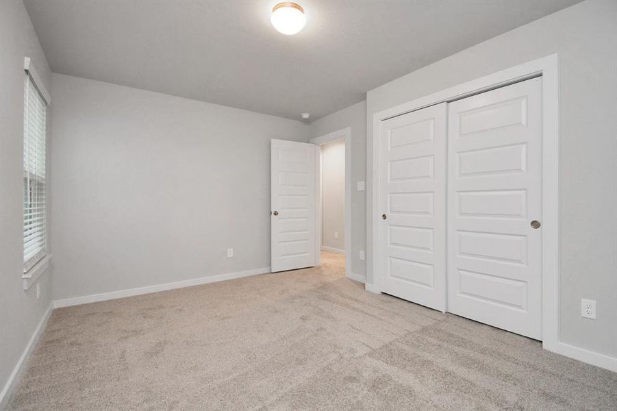 A cozy secondary bedroom with large windows, plush carpet, and spacious closets. The natural light and neutral colors create a serene, inviting atmosphere.