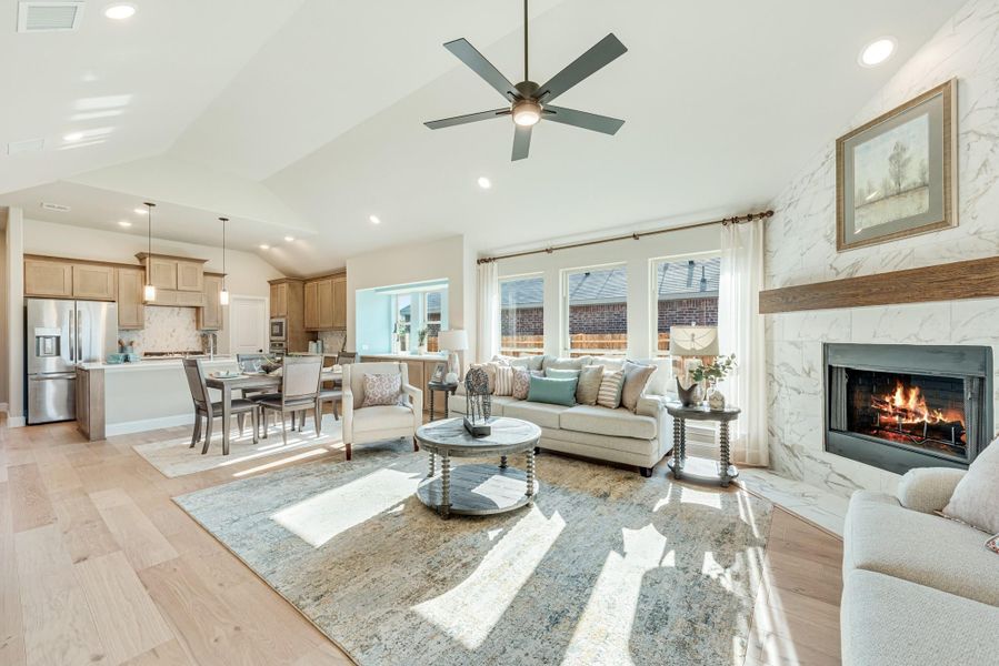 Open-concept living room with vaulted ceiling, marble fireplace, and view into kitchen and dining area