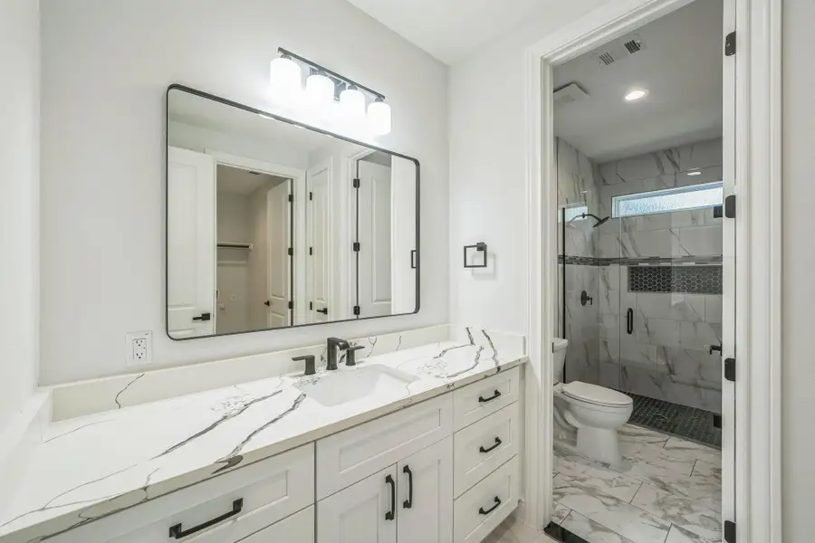 Bathroom featuring vanity, a marble finish shower, light marble finish floors, and recessed lighting