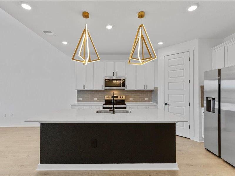 Kitchen with a center island with sink, appliances with stainless steel finishes, white cabinets, decorative light fixtures, and decorative backsplash