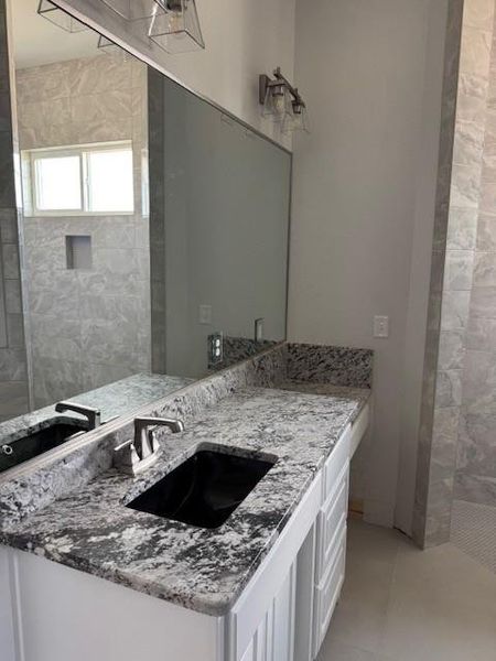 Full bathroom featuring vanity, tiled shower, and light tile patterned floors