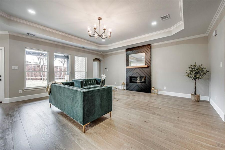 Living room with an inviting chandelier, ornamental molding, a raised ceiling, a fireplace, and hardwood / wood-style floors