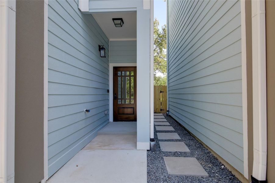 Welcoming covered entry with modern lighting anda wood front door with glass panes. Clean siding,concrete step, and a side paver walkway overgravel leading to the gated backyard—low-maintenance and secure. Welcoming covered entry with modern lighting anda wood front door with glass panes. Clean siding,concrete step, and a side paver walkway overgravel leading to the gated backyard—low-maintenance and secure.