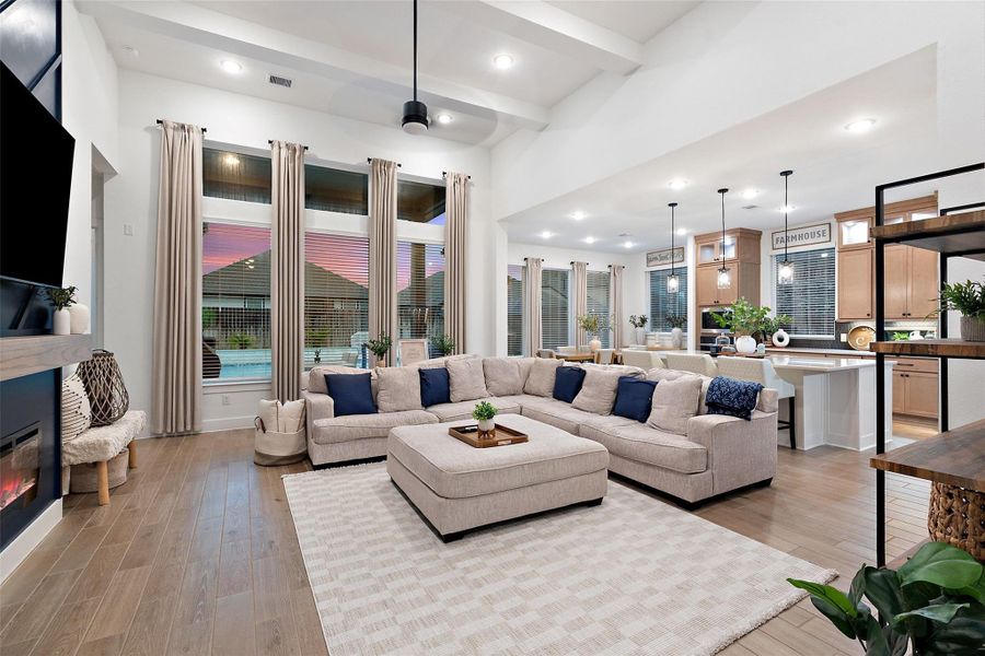 The soaring family room features high ceilings with beams, an electric fireplace wall, and flows into a chef's kitchen with quartz countertops, oversized island, luxe pantry, Barley cabinetry with glass uppers, and GE Profile appliances including double ovens with built-in air fryer. The soaring family room features high ceilings with beams, an electric fireplace wall, and flows into a chef's kitchen with quartz countertops, oversized island, luxe pantry, Barley cabinetry with glass uppers, and GE Profile appliances including double ovens with built-in air fryer.