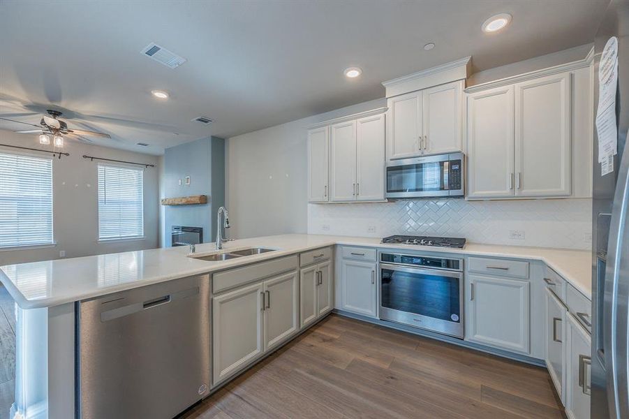 Kitchen featuring quartz peninsula contertops, appliances with stainless steel finish, hardwood flooring and white cabinets with door handles - View