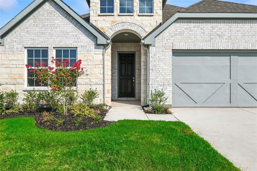 Property entrance featuring an attached garage, stone siding, driveway, roof with shingles, and brick siding Property entrance featuring an attached garage, stone siding, driveway, roof with shingles, and brick siding