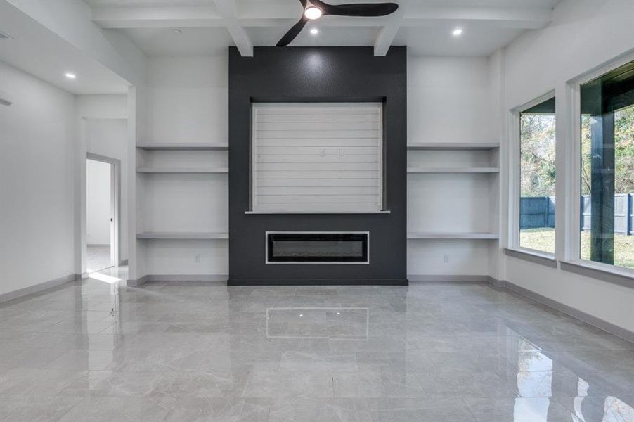 Unfurnished living room featuring beamed ceiling, plenty of natural light, ceiling fan, and a fireplace