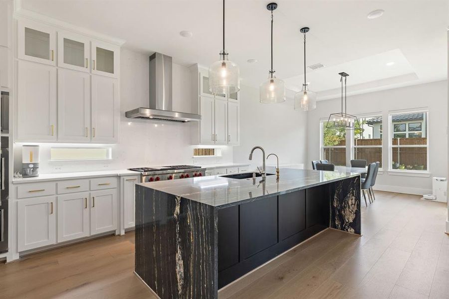 Kitchen with wall chimney range hood, light wood finished floors, white cabinets, a raised ceiling, and recessed lighting