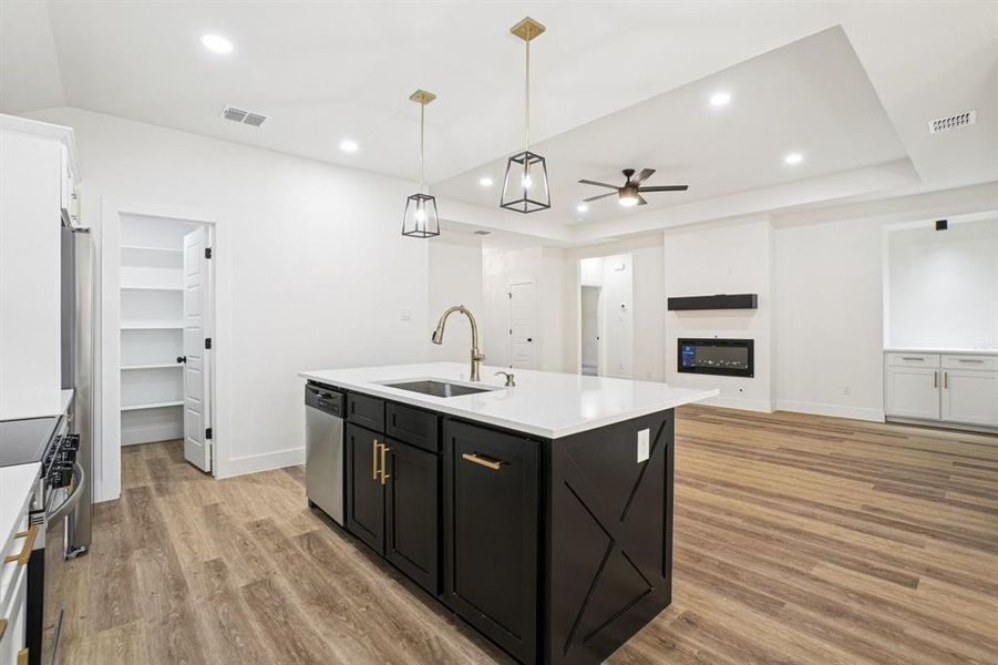 Kitchen featuring dark cabinetry, hanging light fixtures, a center island with sink, open floor plan, and light wood-type flooring Kitchen featuring dark cabinetry, hanging light fixtures, a center island with sink, open floor plan, and light wood-type flooring