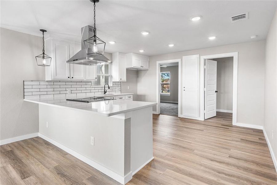 Kitchen with tasteful backsplash, a peninsula, white cabinets, ventilation hood, and recessed lighting