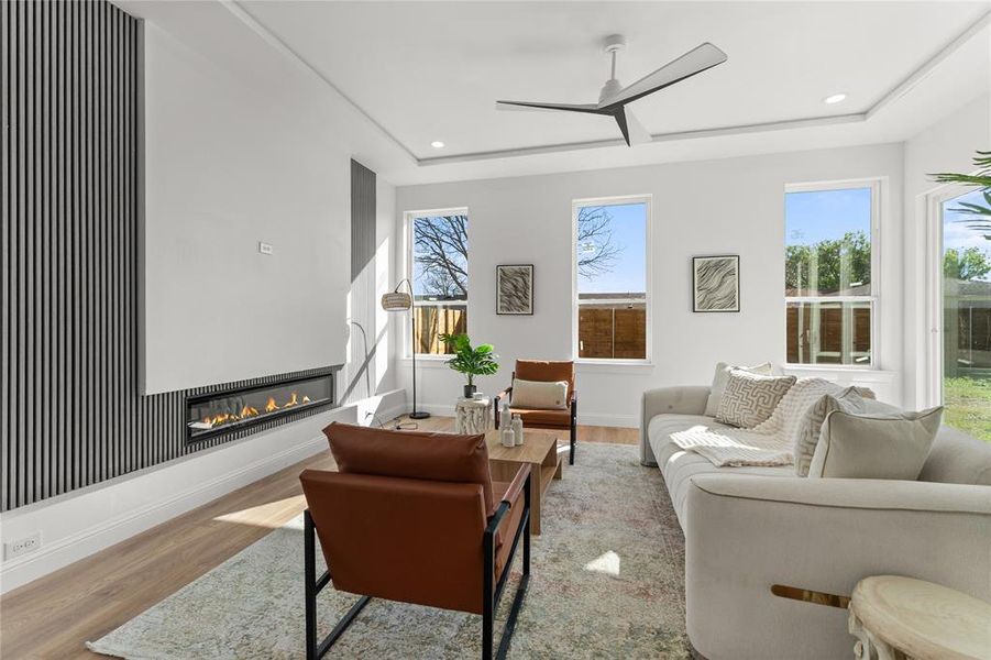 Living area featuring a ceiling fan, a glass covered fireplace, wood finished floors, a raised ceiling, and recessed lighting