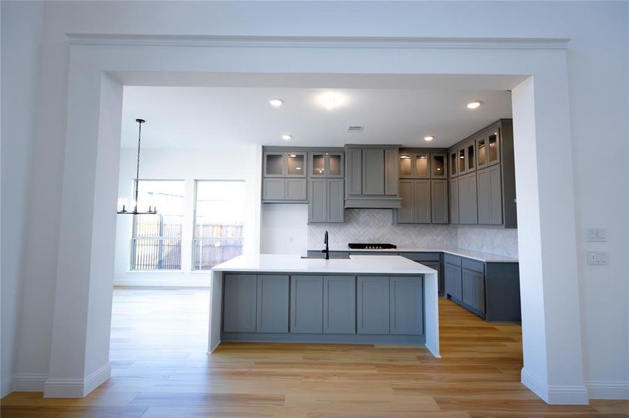 Kitchen featuring a center island with sink, gray cabinets, tasteful backsplash, light wood-type flooring, and recessed lighting Kitchen featuring a center island with sink, gray cabinets, tasteful backsplash, light wood-type flooring, and recessed lighting