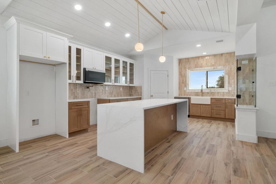 Kitchen with glass insert cabinets, decorative backsplash, vaulted ceiling, light stone countertops, and a center island Kitchen with glass insert cabinets, decorative backsplash, vaulted ceiling, light stone countertops, and a center island