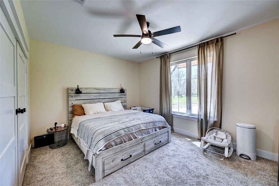 This bedroom features a cozy design with neutral tones, a large window for natural light, and a ceiling fan. It includes a bed with storage drawers and a modest bedside table, creating a comfortable and functional space.