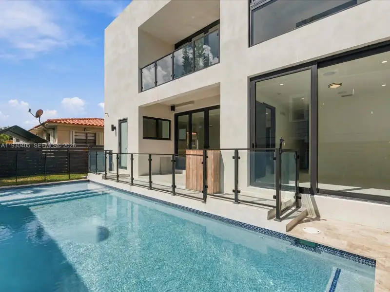 Contemporary two-story exterior featuring smooth stucco siding, large-format sliding glass doors, a second-story balcony with glass railings, and a recessed swimming pool with stone decking Contemporary two-story exterior featuring smooth stucco siding, large-format sliding glass doors, a second-story balcony with glass railings, and a recessed swimming pool with stone decking