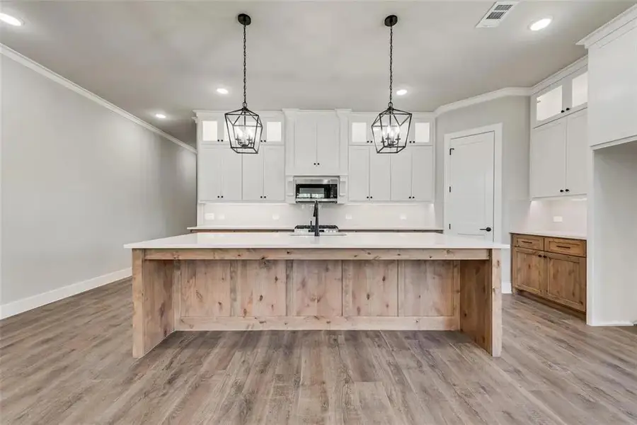 Kitchen featuring decorative backsplash, a large island with sink, dual tone cabinets, stainless steel microwave, and light wood-style flooring