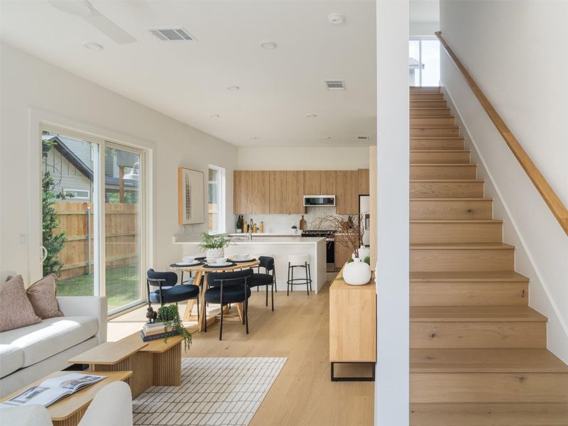 Open-concept living space featuring wood-finish flooring, a contemporary kitchen with light wood cabinetry and a white subway tile backsplash, and a sliding glass door providing access to the backyard