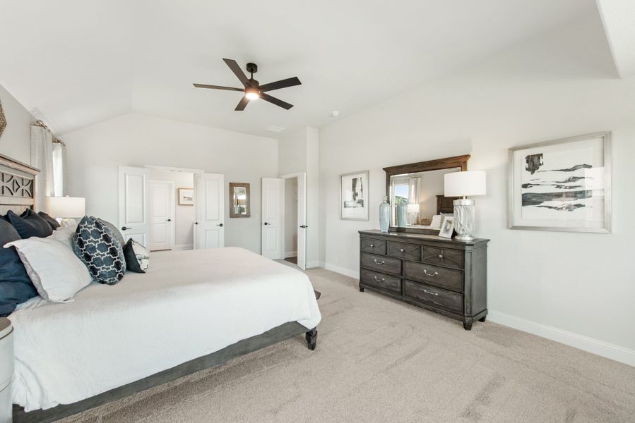 Master bedroom with vaulted ceiling, ceiling fan, dark wood dresser, and carpet flooring