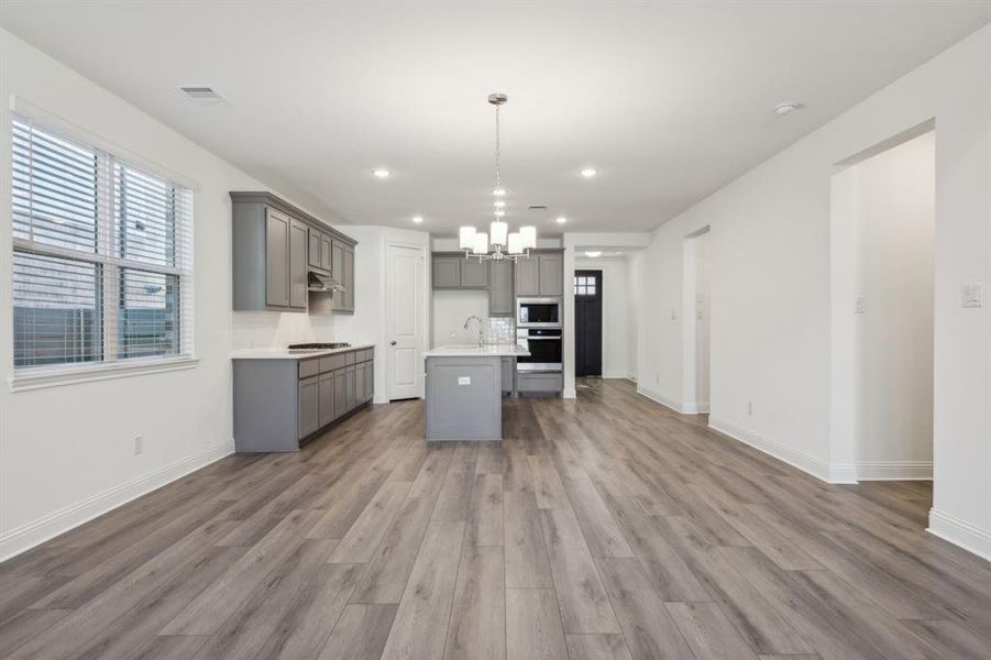 Kitchen featuring hardwood / wood-style floors, pendant lighting, gray cabinets, and an island with sink