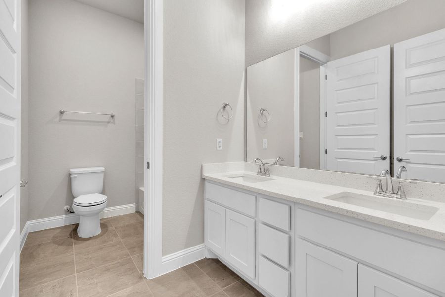 Bathroom featuring double vanity, toilet, baseboards, and a sink Bathroom featuring double vanity, toilet, baseboards, and a sink