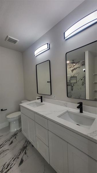 Bathroom featuring double vanity, visible vents, a marble finish shower, and a sink