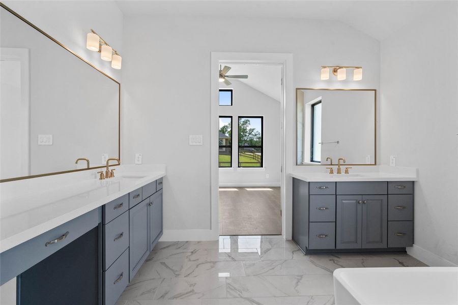 This stunningly updated primary bathroom is truly move-in ready! It features gorgeous painted dual vanity cabinetry with light countertops, large framed mirrors, soaring ceilings, custom paint, and sleek modern fixtures.