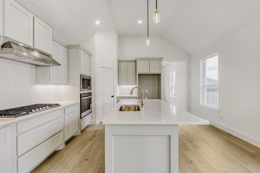 Kitchen with a center island with sink, hanging light fixtures, light wood-style flooring, tasteful backsplash, and lofted ceiling Kitchen with a center island with sink, hanging light fixtures, light wood-style flooring, tasteful backsplash, and lofted ceiling