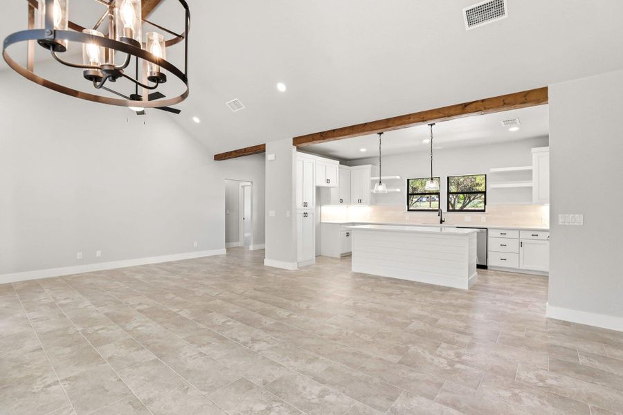 An airy living area transitions seamlessly into a contemporary kitchen, illuminated by recessed lighting and a striking chandelier. An airy living area transitions seamlessly into a contemporary kitchen, illuminated by recessed lighting and a striking chandelier.