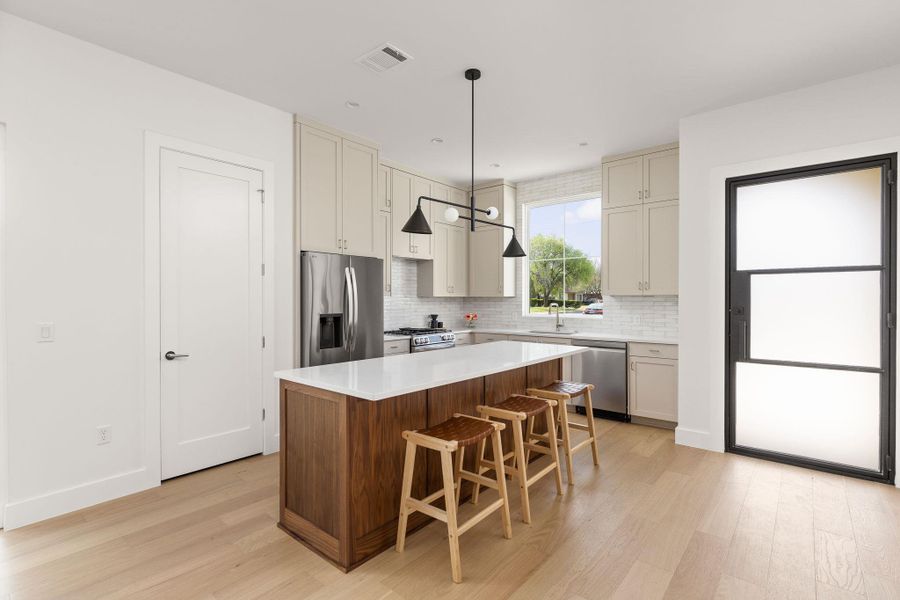 Kitchen featuring a center island, stainless steel appliances, a breakfast bar area, light wood finished floors, and two tone cabinetry Kitchen featuring a center island, stainless steel appliances, a breakfast bar area, light wood finished floors, and two tone cabinetry