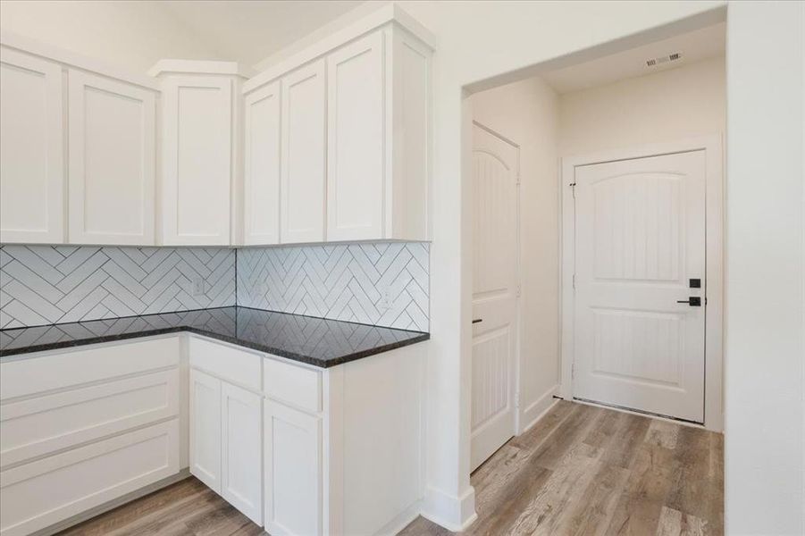 Kitchen featuring tasteful backsplash, white cabinets, light wood-type flooring, and dark counters