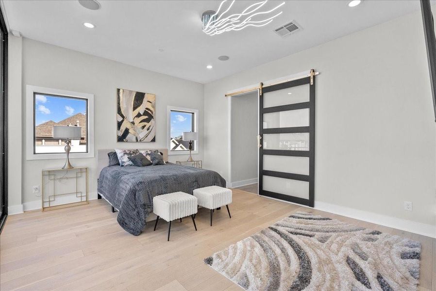 This bedroom features a modern design with light wood flooring, a stylish bed with dark bedding, and two windows providing natural light. A chic sliding door adds a contemporary touch, complemented by abstract artwork and elegant lighting. This bedroom features a modern design with light wood flooring, a stylish bed with dark bedding, and two windows providing natural light. A chic sliding door adds a contemporary touch, complemented by abstract artwork and elegant lighting.