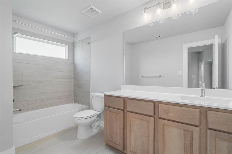 Secondary bath features tile flooring, bath/shower combo with tile surround, white stained wood cabinets, beautiful light countertops, mirror, dark, sleek fixtures and modern finishes.