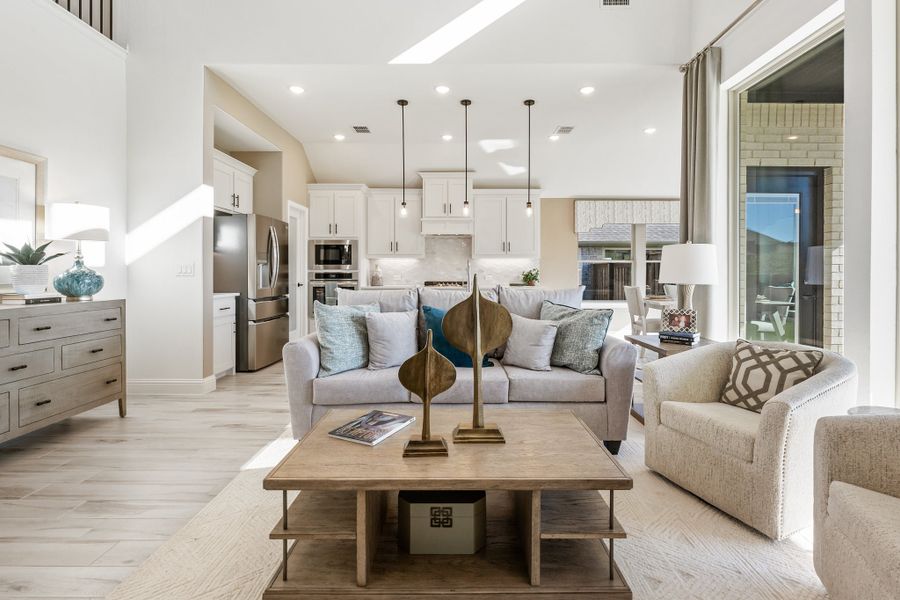 Open-concept living room with gray sofas, wood coffee table, and kitchen visible in background with white cabinets and stainless appliances