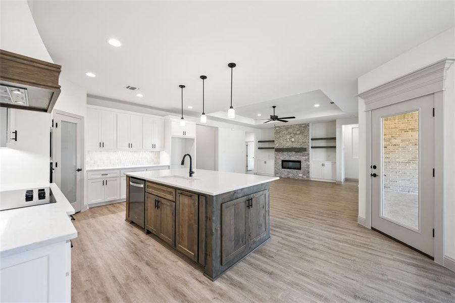 Kitchen with a stone fireplace, a kitchen island with sink, custom range hood, white cabinets, and light wood-type flooring
