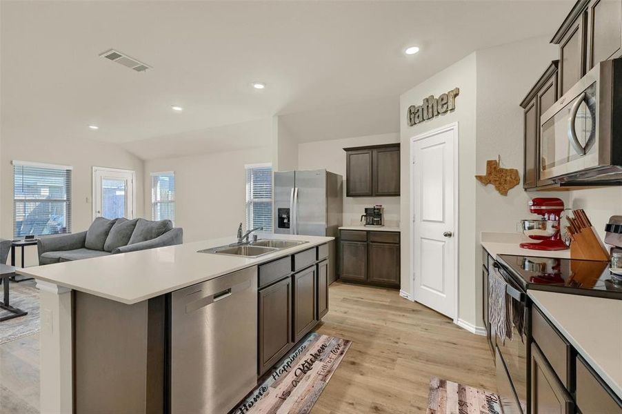 Kitchen featuring dark brown cabinetry, appliances with stainless steel finishes, light hardwood / wood-style floors, sink, and a kitchen island with sink