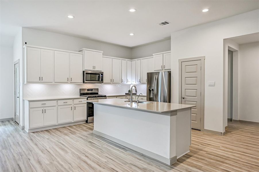 Crisp white cabinetry stretches across the kitchen, complemented by sleek countertops, stainless appliances and a herringbone-pattern tile backsplash. The oversized island adds an abundance of prep space and storage. Crisp white cabinetry stretches across the kitchen, complemented by sleek countertops, stainless appliances and a herringbone-pattern tile backsplash. The oversized island adds an abundance of prep space and storage.