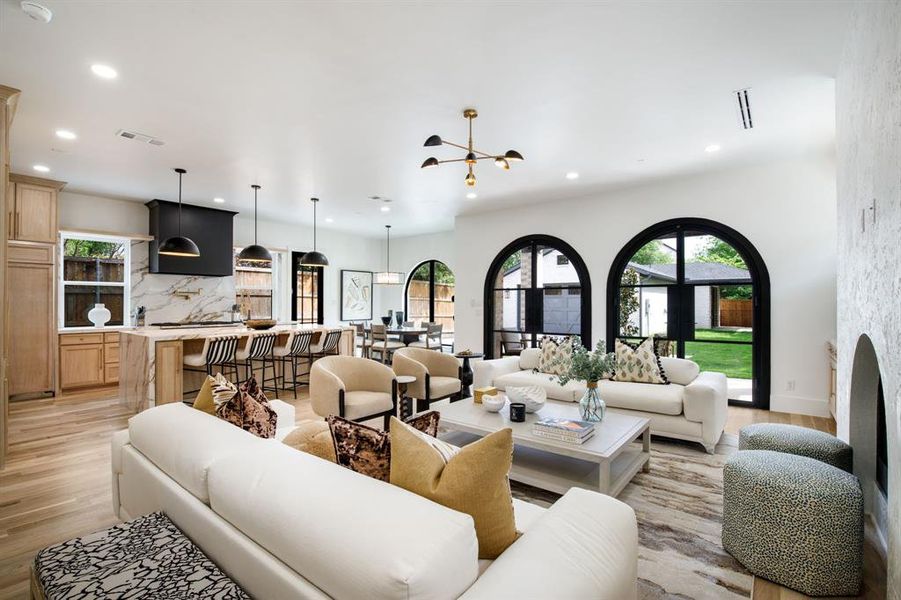 Spacious open-concept living area featuring light wood-finish flooring, a contemporary chandelier, recessed lighting, and a textured white accent wall with an arched niche Spacious open-concept living area featuring light wood-finish flooring, a contemporary chandelier, recessed lighting, and a textured white accent wall with an arched niche