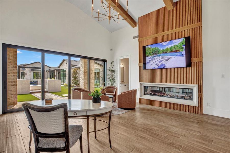 Dining space featuring a chandelier, high vaulted ceiling, wood finish floors, a glass covered fireplace, and beam ceiling Dining space featuring a chandelier, high vaulted ceiling, wood finish floors, a glass covered fireplace, and beam ceiling