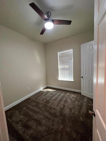 Unfurnished bedroom with dark colored carpet and a ceiling fan
