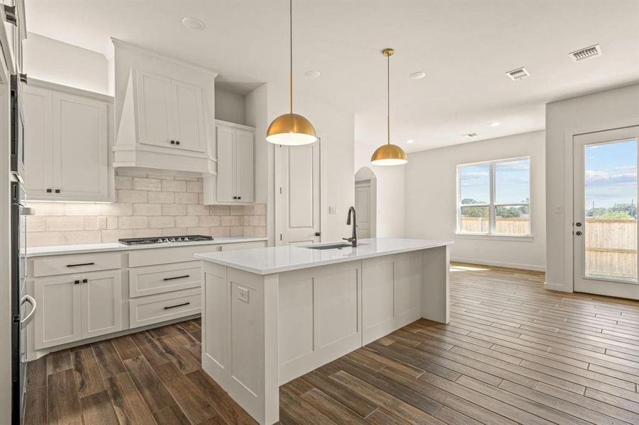 Kitchen with a sink, dark wood-style floors, light countertops, decorative backsplash, and stainless steel gas stovetop