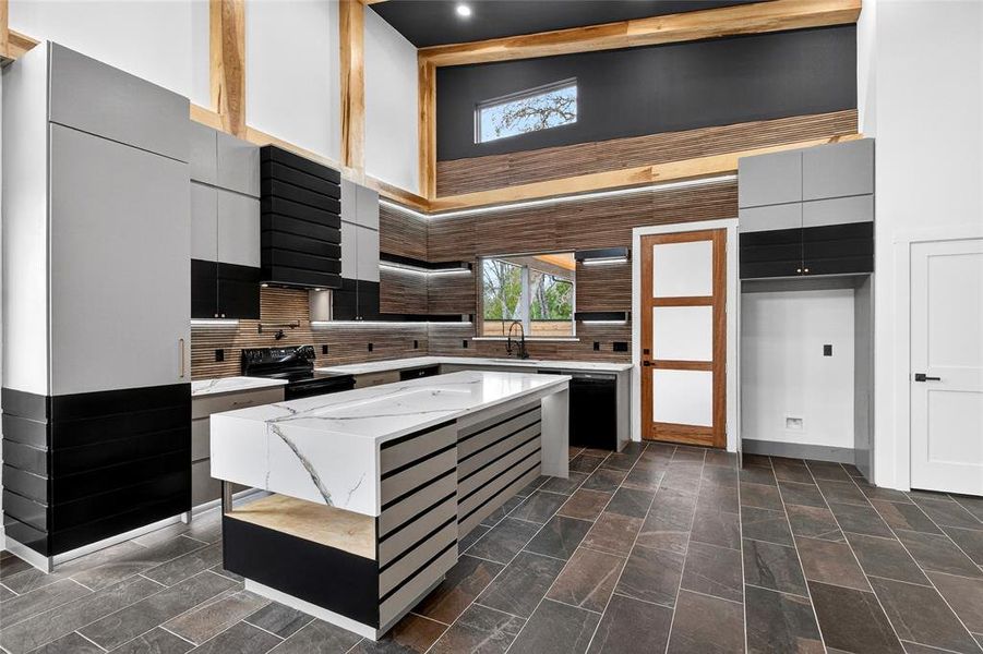 Kitchen featuring modern cabinets, light stone counters, a kitchen island, dual tone cabinetry, and a high ceiling