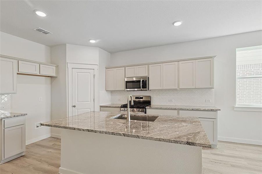 Kitchen featuring light hardwood / wood-style floors, stainless steel appliances, light stone counters, and a kitchen island with sink