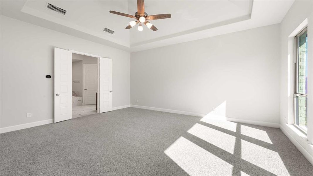 Unfurnished bedroom featuring ceiling fan, a tray ceiling, and multiple windows