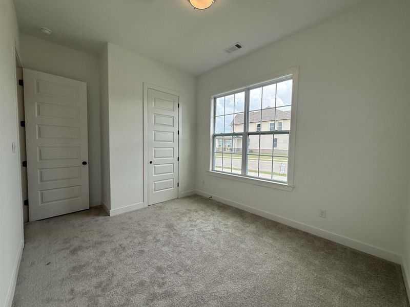 Neutral-toned room featuring a large window with grid-patterned panes, light gray carpeting, and white walls