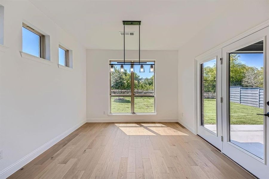 Open-concept area featuring light wood-finish flooring, white walls, and a contemporary linear chandelier with glass shades Open-concept area featuring light wood-finish flooring, white walls, and a contemporary linear chandelier with glass shades