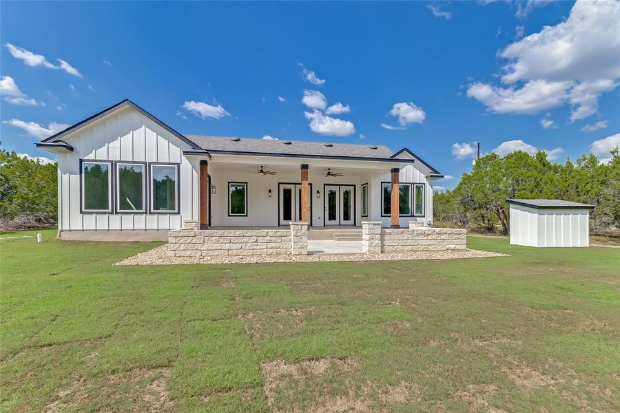 Back of house featuring a ceiling fan, board and batten siding, a patio area, a lawn, and french doors