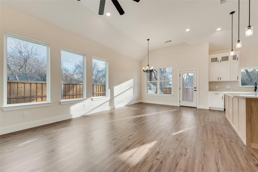 Unfurnished living room with light wood finished floors, a chandelier, ceiling fan, high vaulted ceiling, and recessed lighting