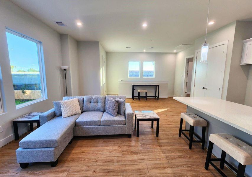 This spacious living area features a modern open layout with abundant natural light, a cozy sectional sofa, sleek hardwood floors, and a stylish breakfast bar with seating. Perfect for comfortable living and entertaining. This spacious living area features a modern open layout with abundant natural light, a cozy sectional sofa, sleek hardwood floors, and a stylish breakfast bar with seating. Perfect for comfortable living and entertaining.