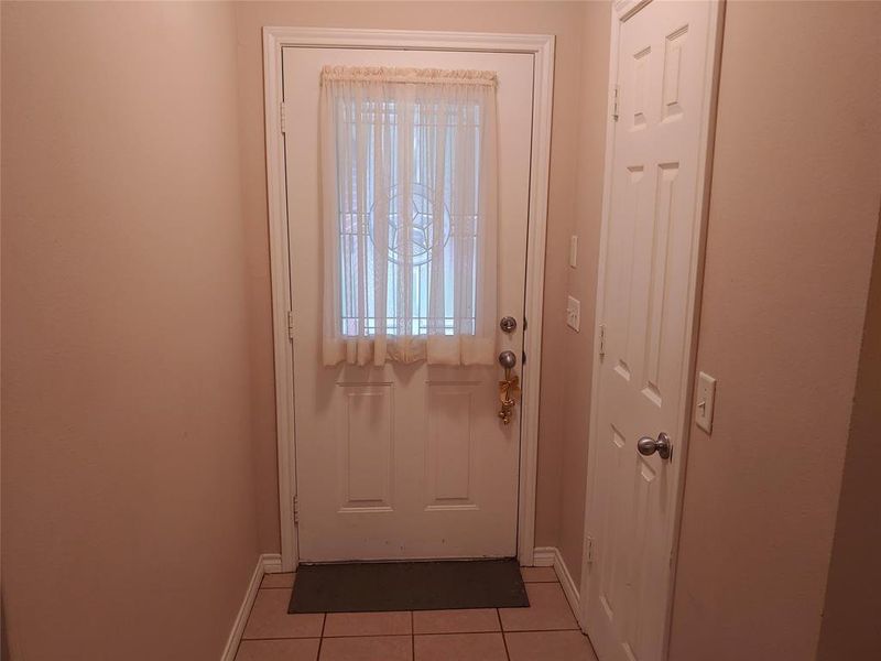 Entryway featuring a white door with decorative glass inserts, ceramic tile flooring, and a paneled utility door