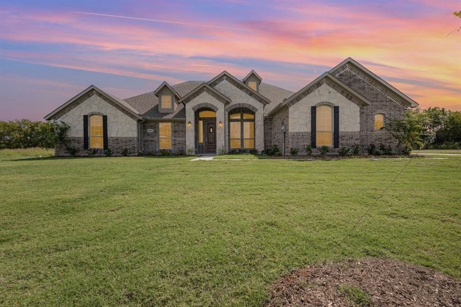 French country home with stone siding, a lawn, roof with shingles, and brick siding French country home with stone siding, a lawn, roof with shingles, and brick siding